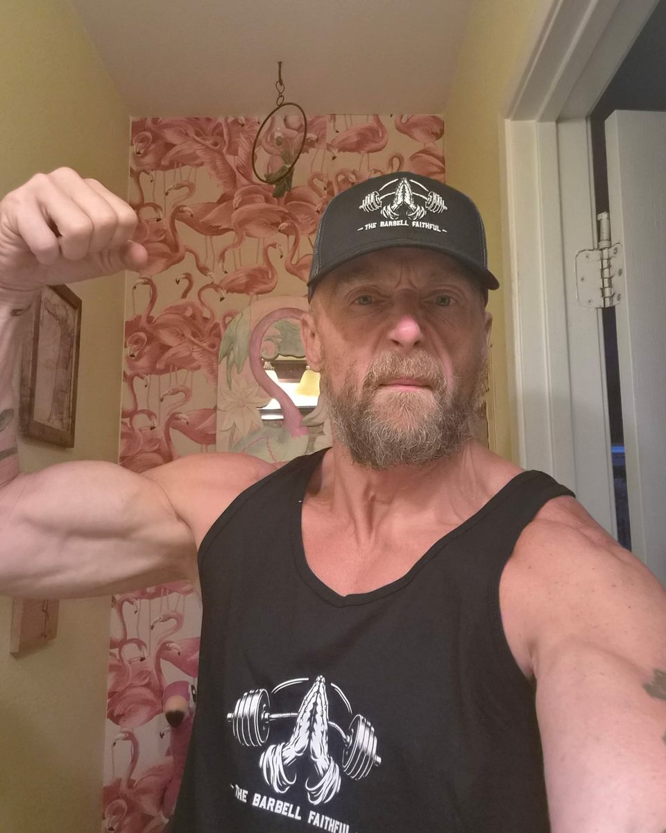 Coach Richard flexing in the black and charcoal Barbell Faithful trucker hat and black tank